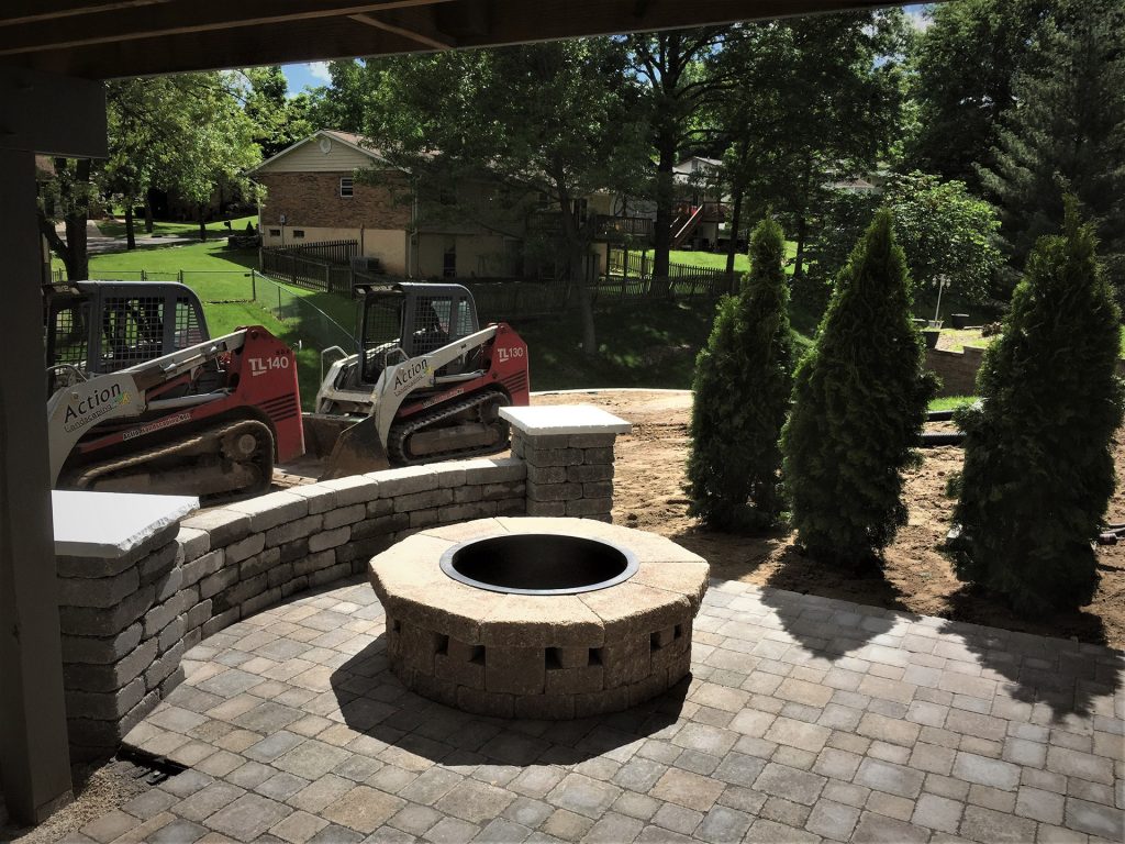 round tumbled block wood burning fire pit constructed a top a paver patio in Concord Saint Louis Missouri accented by curved sitting wall with two decorative columns created by Action Landscaping